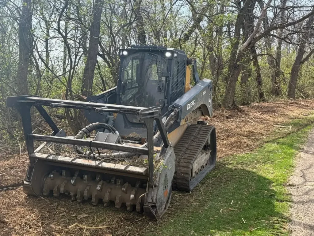 Reclaim Land Services skid steer with forestry mulcher head at the edge of a woodlot