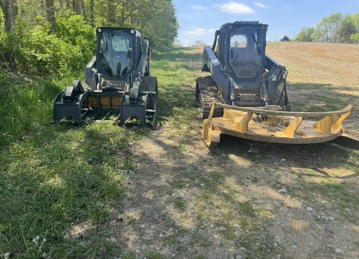 Skid steers with attachments staged at a field edge near Dayton, OH